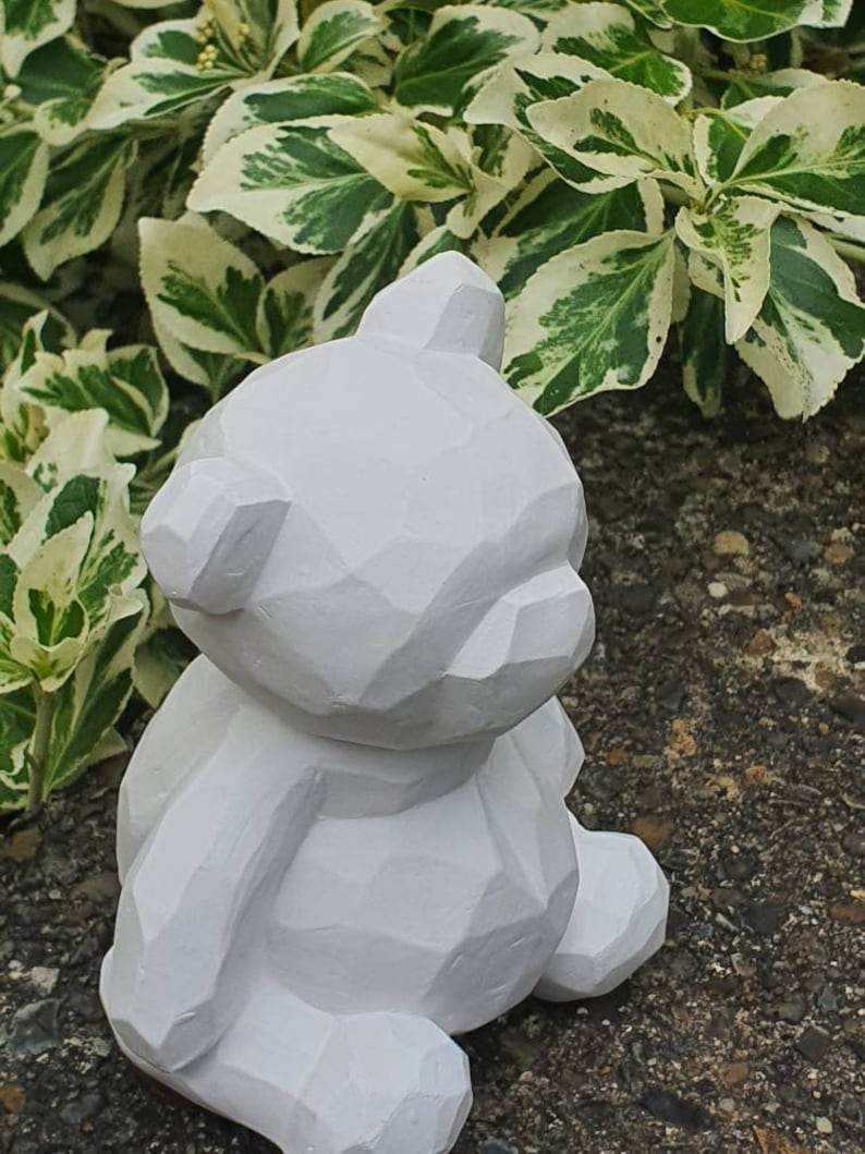 K&ouml;nnte beinhalten: Eine wei&szlig;e, geometrisch geformte Teddyb&auml;r-Figur. Der B&auml;r sitzt mit gekreuzten Beinen und hat ein schlichtes, modernes Design.