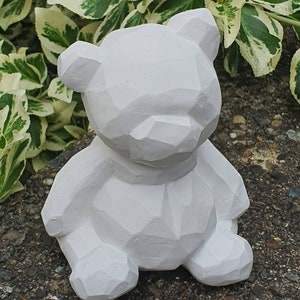K&ouml;nnte beinhalten: Eine wei&szlig;e geometrische Teddyb&auml;r-Figur. Der B&auml;r sitzt mit gekreuzten Beinen und hat ein schlichtes, modernes Design.