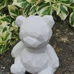 K&ouml;nnte beinhalten: Wei&szlig;e geometrische B&auml;renfigur mit strukturierter Oberfl&auml;che. Der B&auml;r sitzt auf einer grauen Oberfl&auml;che.