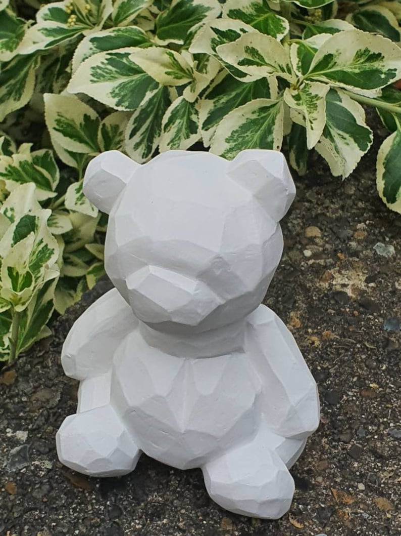 K&ouml;nnte beinhalten: Wei&szlig;e geometrische B&auml;renfigur mit strukturierter Oberfl&auml;che. Der B&auml;r sitzt auf einer grauen Oberfl&auml;che.