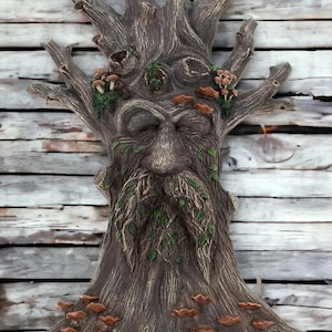 Könnte beinhalten: Eine Holzskulptur eines Baumes mit einem Gesicht, einem Bart und Pilzen, die darauf wachsen. Die Skulptur ist in Braun-, Grün- und Weißtönen bemalt.
