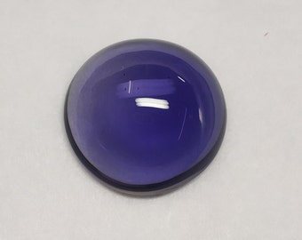 May include: A round, cabochon-cut amethyst gemstone with a deep purple hue. The stone is smooth and polished, with a slight sheen.