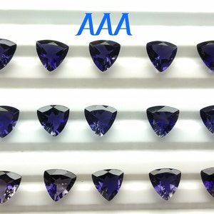 May include: Twelve triangular, faceted, dark purple gemstones arranged in three rows of four on a white surface. The text "AAA" is printed in blue above the gemstones.
