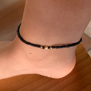 May include: A black beaded ankle bracelet with two gold beads.