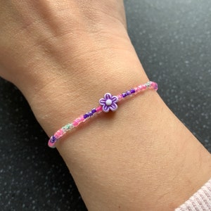 Op de afbeelding: Een roze en paarse kralen armband met een paarse bloem bedel.