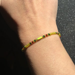 May include: A yellow, red, and green beaded bracelet with a single larger yellow bead in the center.