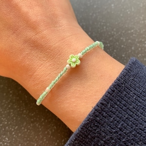 May include: A delicate green and white beaded bracelet with a small green flower charm.