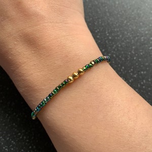 Op de afbeelding: Een delicate armband gemaakt met iriserende groene en gouden kralen. De armband is simpel en elegant, perfect voor dagelijks gebruik.