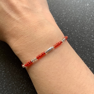May include: A red and silver beaded bracelet with small silver beads interspersed throughout the red beads.
