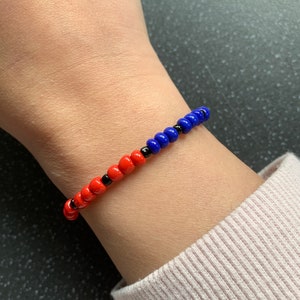 May include: A red, blue, and black beaded bracelet on a person's wrist.