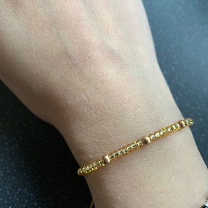 May include: A gold beaded bracelet with small, round, yellow beads and larger, round, gold beads.