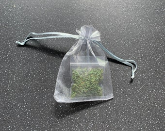 Puede incluir: Una pequeña bolsa de malla blanca llena de hierbas secas. La bolsa está atada con una cinta azul.