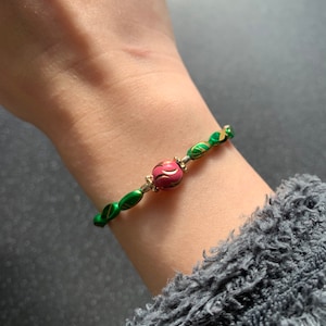 May include: A green and gold beaded bracelet with a pink and gold bead in the center.