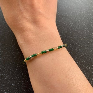 Puede incluir: Un brazalete de cuentas verdes y doradas en la muñeca de una persona.