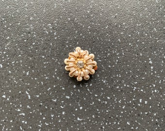 May include: A small gold-toned flower brooch with white pearl accents and a clear rhinestone center.