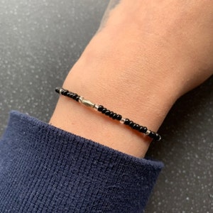 May include: A simple black and silver beaded bracelet with a silver clasp. The bracelet is worn on a person's wrist.