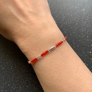 May include: A simple bracelet made with small orange and silver beads. The bracelet is worn on a person's wrist.