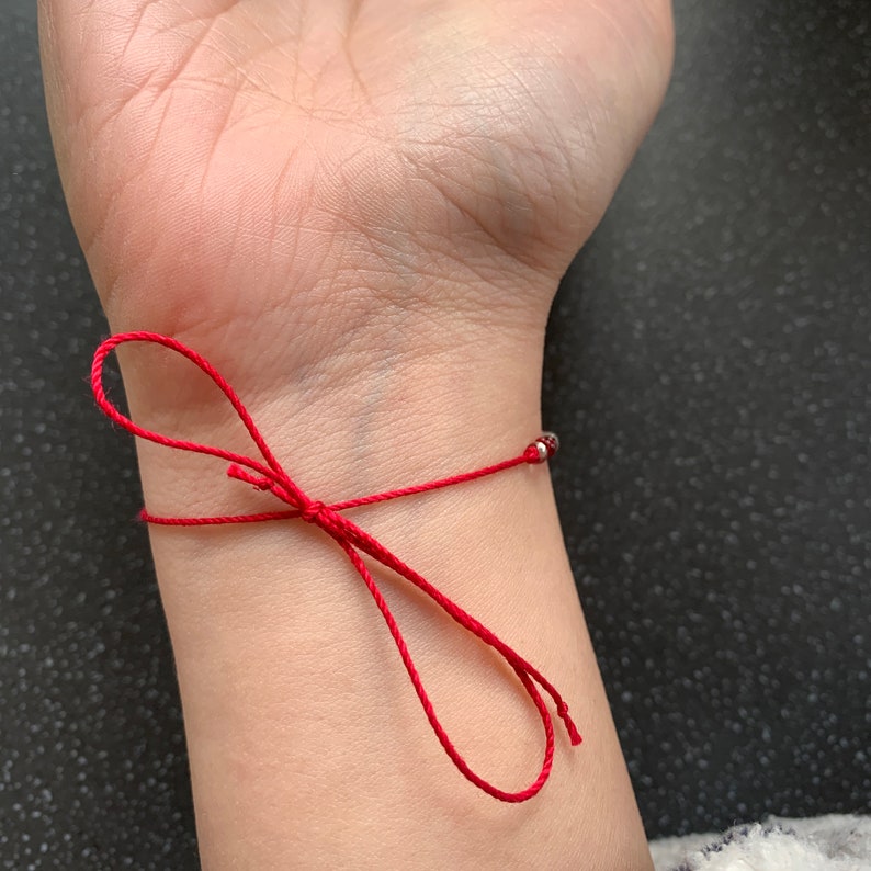 May include: A red string bracelet with small silver beads on a person's wrist.