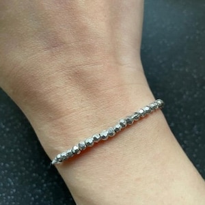 May include: A silver bracelet with small, round beads. The bracelet is on a person's wrist.