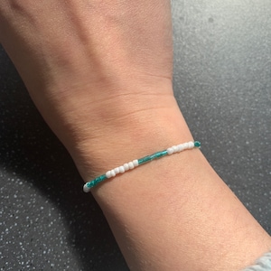 May include: A simple bracelet made with white and teal beads.