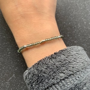 May include: A silver and green beaded bracelet on a person's wrist.