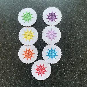 May include: Seven white circles with scalloped edges, each containing a star-shaped design in a different colour: green, yellow, purple, light purple, orange, blue, and red.