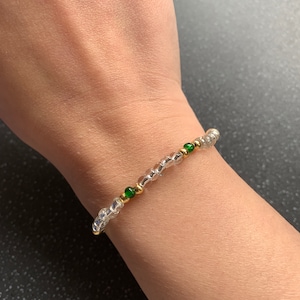 May include: A silver and gold beaded bracelet with green accent beads.