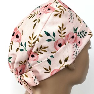 May include: A light pink surgical scrub cap with a floral pattern. The cap features a repeating design of pink roses, green leaves, and brown stems. The cap is tied at the back.