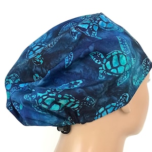 May include: Blue and green surgical scrub hat with a pattern of sea turtles. The hat has an adjustable back strap.