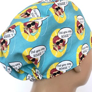 May include: A turquoise blue scrub hat with a repeating pattern of a cartoon woman with red hair wearing sunglasses and a yellow sunburst. The text "Did you say BOUGIE?" is in a speech bubble above the woman's head.