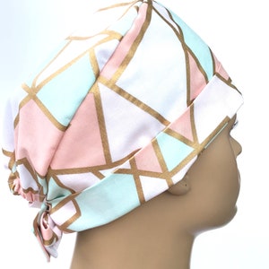 May include: A surgical scrub hat with a geometric pattern in shades of pink, mint green, and gold. The hat is tied at the back.