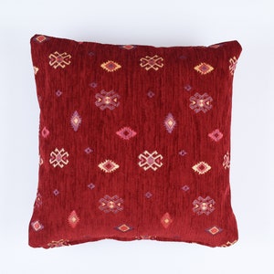 Puede incluir: Una almohada roja con un patrón geométrico en tonos de rosa, crema y azul.
