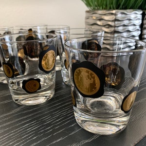 May include: Set of six clear glass tumblers with black and gold coin designs. The glasses have a vintage look and are perfect for serving drinks.