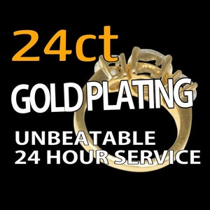 May include: A gold ring with three diamonds set in the band. The ring is on a black background with the text "24ct GOLD PLATING UNBEATABLE 24 HOUR SERVICE".