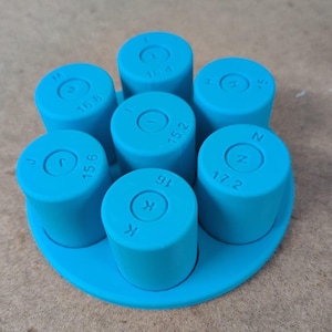 May include: A bright blue ring sizing tool set featuring six cylindrical pieces arranged on a circular base. Each cylinder is marked with a letter and a numerical value, including 15.2, 15.4, 15.6, 16, 16.8, and 17.2, indicating specific ring sizes.