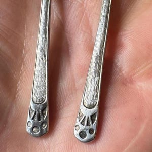 Peut inclure: Gros plan sur deux cuillères en argent. Les cuillères ont un motif texturé sur les manches et des motifs décoratifs près du bol. Les bols ont un motif circulaire. Les cuillères sont probablement vintage ou antiques.