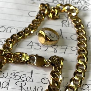 May include: A gold-colored curb chain bracelet with a matching signet ring. The bracelet has a secure clasp. The ring is oval-shaped. The jewelry is displayed on a piece of paper with handwritten notes.