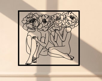 May include: Black and white line art print of three figures with flowers for heads. The figures are sitting together with their legs crossed. The print is framed in a black frame and hanging on a white wall.