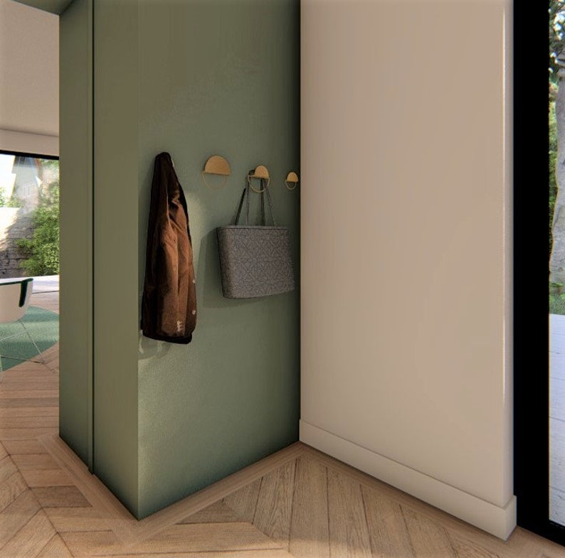 Peut inclure: Un mur vert avec une veste marron et un sac cabas gris accroch&eacute;s &agrave; des crochets dor&eacute;s. Le mur est dans un couloir avec un sol en bois.