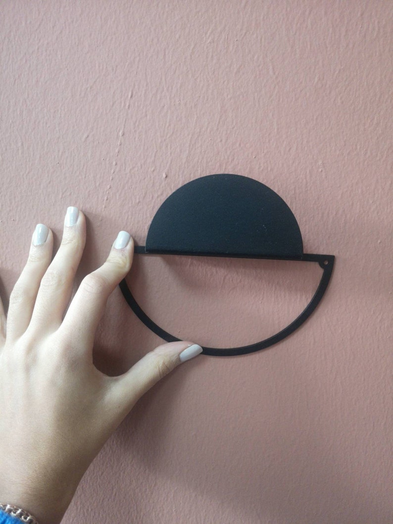 Peut inclure: D&eacute;coration murale en m&eacute;tal noir en forme de demi-cercle avec un cercle plus petit sur le dessus. La d&eacute;coration est mont&eacute;e sur un mur rose.