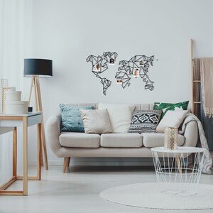 May include: A white sofa with pillows in a living room setting. A black metal world map with photos pinned to it hangs on the wall. A white wire basket coffee table sits in front of the sofa.