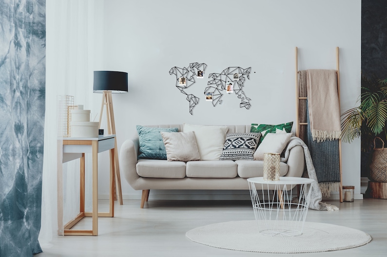 May include: A white sofa with pillows in a living room setting. A black metal world map with photos pinned to it hangs on the wall. A white wire basket coffee table sits in front of the sofa.