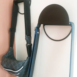 Peut inclure: Deux crochets muraux en m&eacute;tal noir avec des sommets arrondis. Un crochet a un sac &agrave; motifs noir et gris suspendu. L'autre crochet a une sangle bleue et noire suspendue.