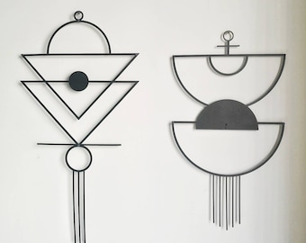 Può includere: Due sculture da parete in metallo nero con forme geometriche e fili pendenti. La scultura a sinistra presenta un cerchio, triangoli e una linea. La scultura a destra presenta un cerchio, semicerchi e una linea.