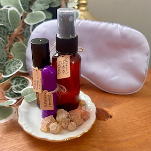 May include: A selection of sleep aids, featuring a brown bottle, a purple inhaler, and a red spray bottle, all with handwritten labels. A white eye mask and a small plate with incense are also present. The labels read "Ashe Somnus 10 ml", "Somnus Aura 50ml", and "Somnus Inhaler".