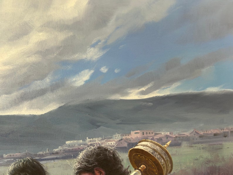 May include: A person with long dark hair is carrying a large, golden prayer wheel. The wheel is decorated with intricate carvings and is set against a backdrop of a distant town and a cloudy sky.