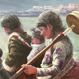 May include: A woman in a floral patterned shirt carries a child on her back while holding a long wooden stick with a metal prayer wheel attached. The woman is wearing a red and white scarf and a white shawl. The child is wearing a white shirt and a white hat.
