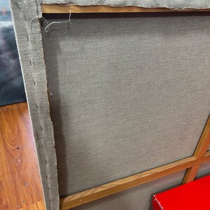 May include: The back of a canvas painting with a wooden frame. The canvas is stretched tightly over the frame and is secured with staples. The frame is made of natural wood and has a light brown color.