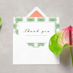 May include: A white envelope with a thank you card inside. The card has a green and white tropical leaf pattern border. Two pink and green anthurium flowers are on either side of the envelope.