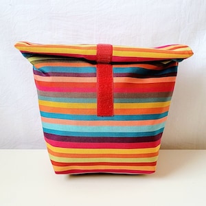 Eine bunt gestreifte Lunchbag mit Innenfutter aus abwaschbarer beschichteter Baumwolle rot weiß gepunktet.Die Lunchbag ist 30 cm hoch, 28 cm breit und 10 cm tief.Zum  Auf und Zumachen ist ein rotes Klettband aufgenäht.